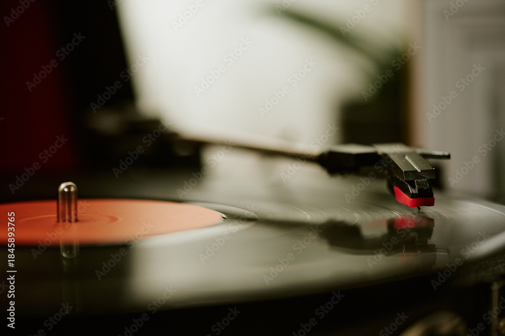 Obraz premium Close up showing vinyl record spinning on turntable with stylus arm lowered, capturing detail of analog music playback, blurred background emphasizing focus on audio equipment