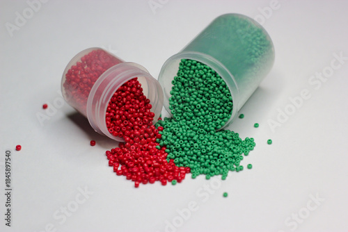 Red and green beads spill out of a jars on white background. Green and red beads. Beads splash out of jar. Beads for jewelry, embroidery, handmade, craft. Hobbie materials