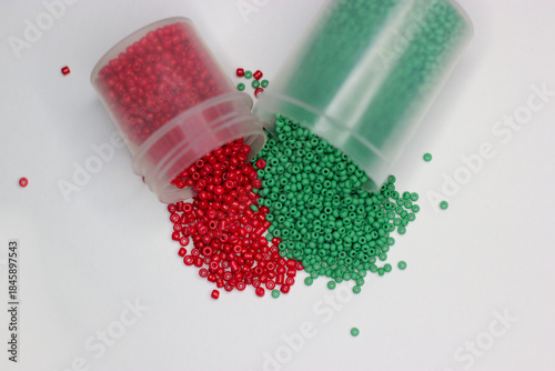 Red and green beads spill out of a jars on white background. Green and red beads. Beads splash out of jar. Beads for jewelry, embroidery, handmade, craft. Hobbie materials