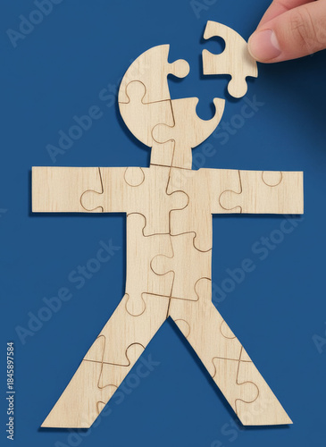 Mental health. A human figure constructed from puzzle pieces, but with one head piece detached from the body and being reattached by the fingers of a mental health professional. Image created using AI