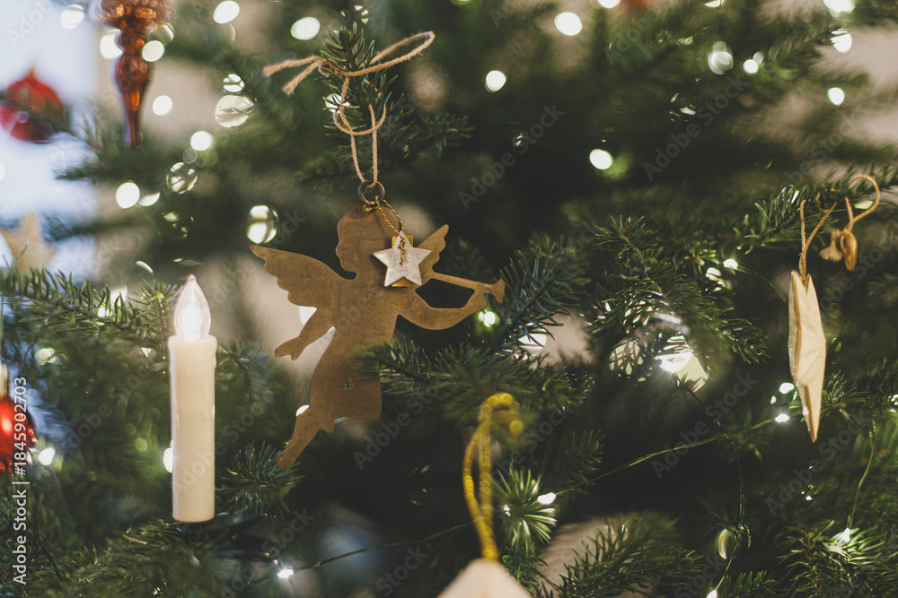 Obraz premium VIntage christmas angel toy hanging on xmas tree branch with festive lights. Happy New Year and Happy Holidays! ! Copy space. Stylish ornament