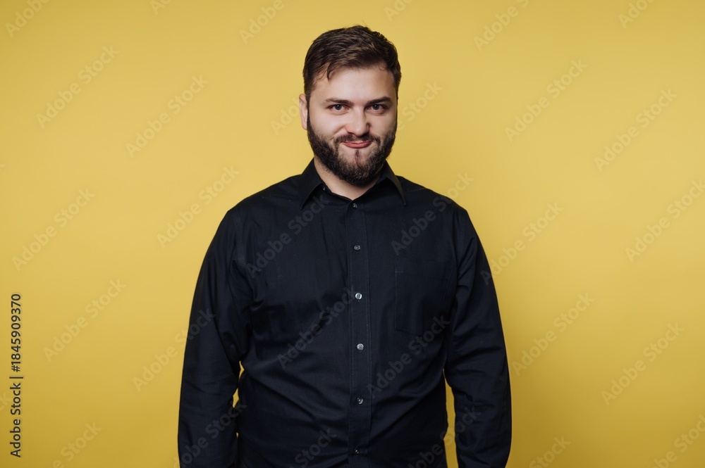 Fototapeta premium Man smiles against yellow background while wearing black shirt and standing with neutral pose in studio setting
