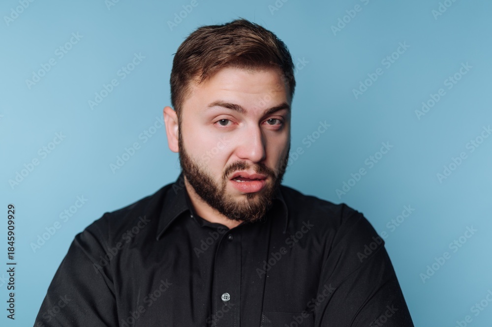 Obraz premium Man with dark shirt shows expression against light blue background in studio setting during daytime