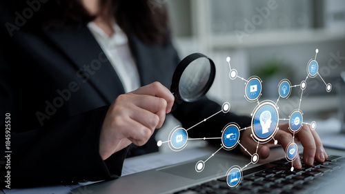 A business professional uses a magnifying glass to examine data on a laptop while surrounded by various digital network icons, symbolizing innovation and insights in the workplace. Tessel