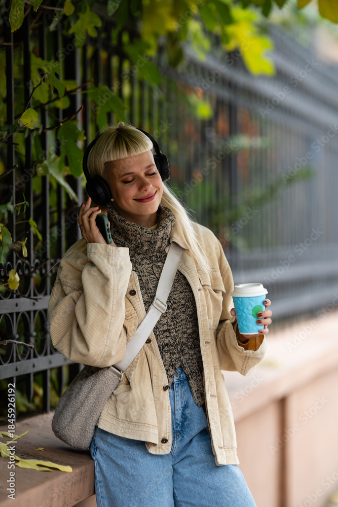 Fototapeta premium Woman enjoying music and coffee on autumn street