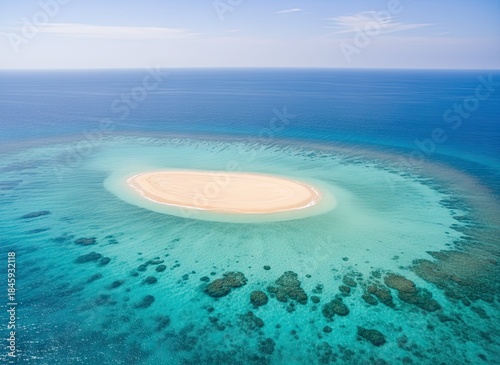 Aerial View Of A Small Tropical Sand Island Surrounded By Turquoise Ocean Water And Coral Reefs Under A Bright Blue Sky
