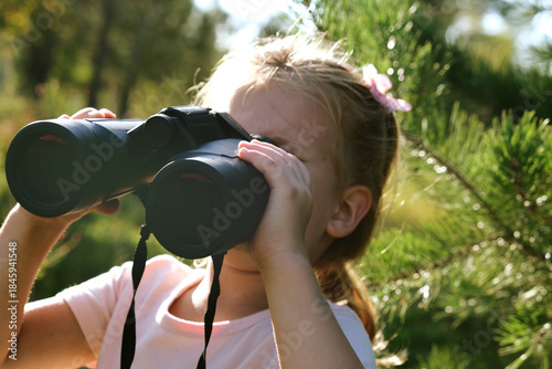 Fotografie Young preschool girl using binoculars in the forest