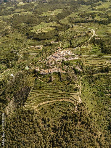 Drone photo of a traditional village surrounded by terraced fields and green hills in South Spain, ideal for travel, agriculture, and rural landscape concepts.