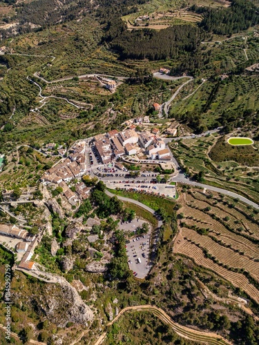 Stunning drone photo of a traditional Spanish village nestled in the mountains of southern Spain, surrounded by lush terraced fields, winding roads, and scenic countryside.