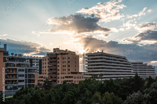 Contemporary residential buildings in South Spain cityscape with dramatic sunset sky, lush greenery, and urban atmosphere. Ideal for real estate, travel, or architecture themes.