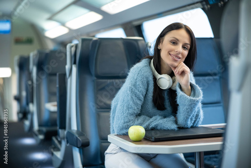 Konstfotografi A smiling woman poses with an apple and laptop in a train, representing healthy eating and modern convenience, highlighting comfort in travel, and ease of working