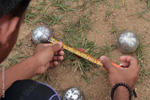 Close-up view of a player measuring the distance between metal petanque balls and the jack using a tape measure on a gravel court. Concept of accuracy, rules, and fair play in traditional outdoor spor