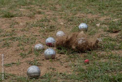 Action shot of metal petanque balls hitting a sandy field, creating flying dirt and dust. Dynamic moment capturing motion, power, and excitement in an outdoor petanque match.