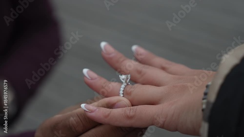 CloseUp Hands With Engagement Ring, Partner Sliding Diamond Band Onto Finger During Intimate Outdoor Proposal On Wooden Boardwalk,