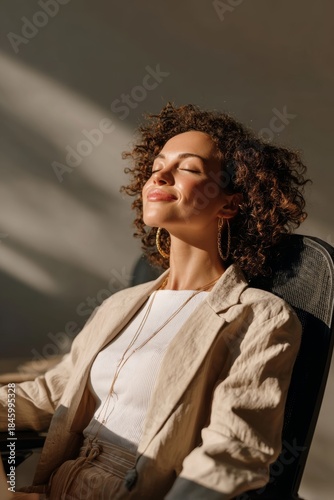 Woman enjoying a moment of relaxation while sitting at her desk during daylight hours in a bright, simple office space