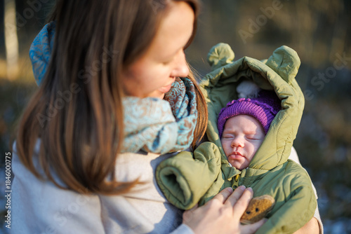 A girl with a child in a sunny winter forest. A mother holds her daughter in a park. The woman smiles at her newborn. The baby is wearing a winter jacket.
