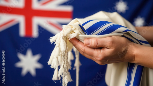 A person holding a traditional Jewish tallit with blue stripes, symbolizing cultural heritage, in front of the Australian flag, reflecting the blend of tradition and national identity.
