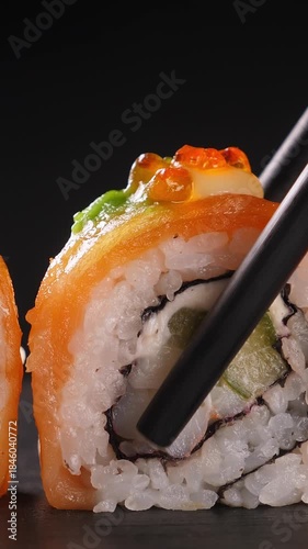 Take one sushi roll from black slate platter using chopsticks, Closeup. Vertical footage
