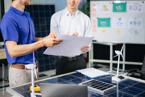 Engineers discuss solar panels and turbines in office, working on clean energy design, sustainable power,