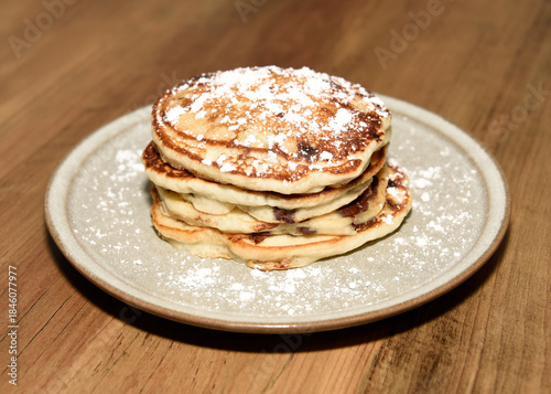 Stack of chocolate chip pancakes on a plate with powdered sugar