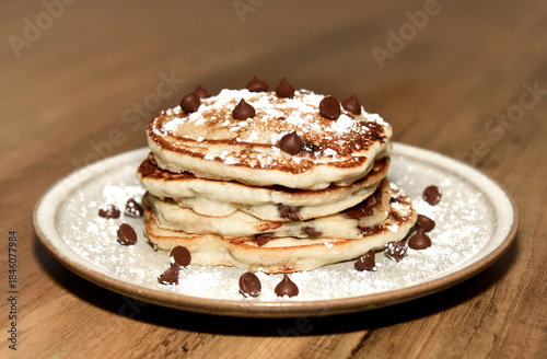 Stack of chocolate chip pancakes on a plate with powdered sugar