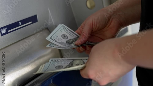 Hands holding several US hundred dollar bills in front of ATM. Person counting cash after withdrawal at bank machine as personal finance and money management concept