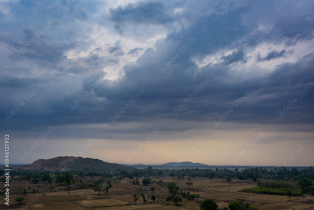 Fototapeta premium Dramatic monsoon clouds over quiet rural landscape at dusk