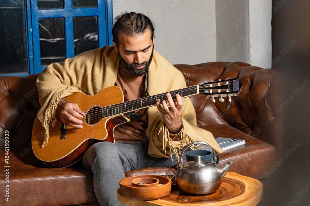 Obraz premium Person playing guitar with mug and teapot on table in intimate indoor setting