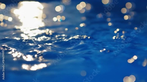 Close-up of sparkling blue water surface with bright sun reflections and soft ripples