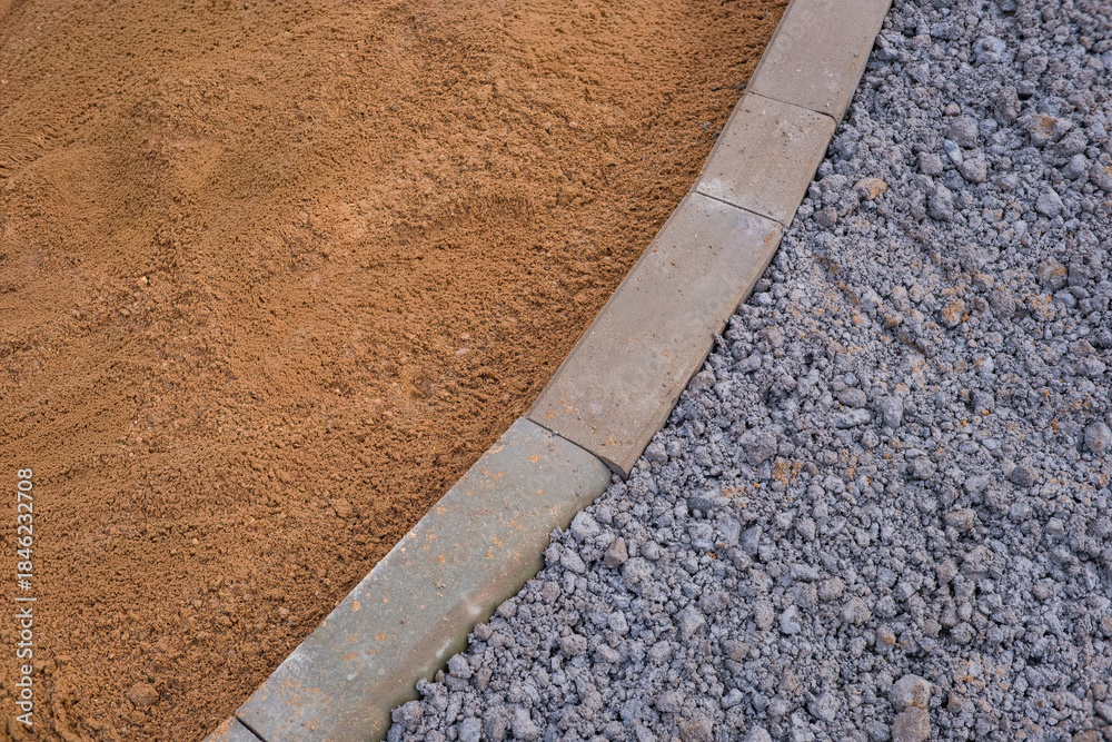 Obraz premium Abstract close-up of sidewalk construction materials. Sand, gravel, and concrete curb form contrasting textures and colors, showing road paving and urban infrastructure work.