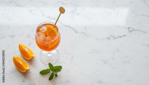 An elegant orange spritz cocktail, a refreshing summer aperitif drink with fresh citrus and ice in a glass, is presented on a minimalist white marble tabletop with copy space.