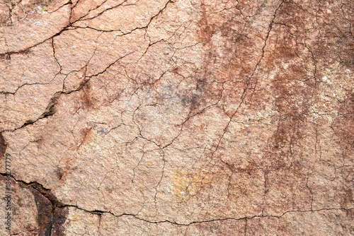 Close-up of natural stone surface texture with cracks and weathered details. Abstract rocky background showing aged mineral patterns and rough stone structure.