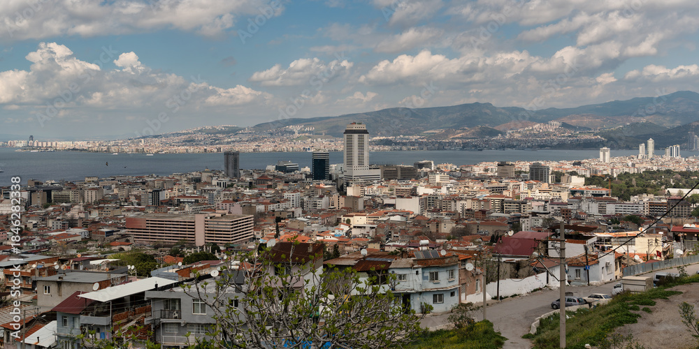 Naklejka premium Panoramic view of Izmir city skyline and Gulf of Izmir, Turkey. Urban landscape with buildings, hills, and cloudy sky