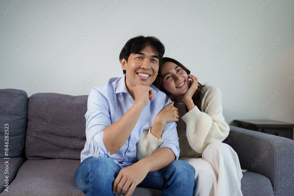 Obraz premium Happy asian couple smiling sitting together on sofa