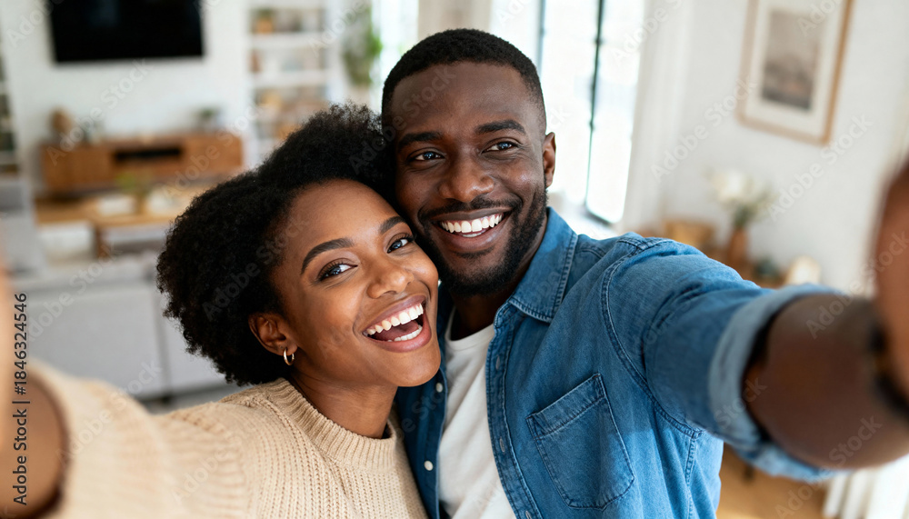Obraz premium Happy young black couple taking a selfie at home. Smiling man and woman looking at the camera together. Portrait of a loving relationship and domestic life