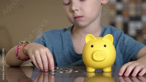 Young boy carefully inserting coins into a yellow piggy bank, illustrating the concept of saving money for the future, financial literacy, and early investment habits at home