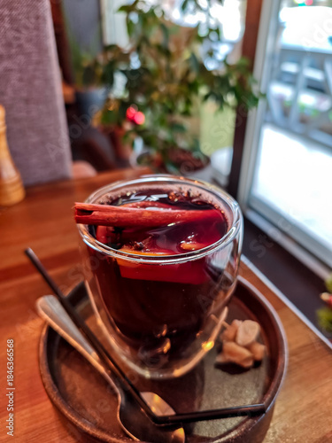 Close-up of mulled wine in a glass cup with cinnamon stick, cloves and orange slices. Traditional hot spiced red wine, cozy winter drink served in a café, perfect for Christmas and holiday atmosphere.