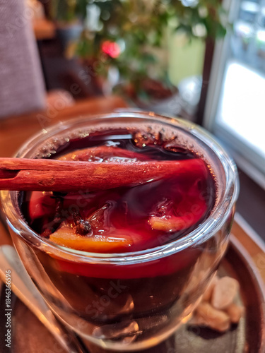 Close-up of mulled wine in a glass cup with cinnamon stick, cloves and orange slices. Traditional hot spiced red wine, cozy winter drink served in a café, perfect for Christmas and holiday atmosphere.