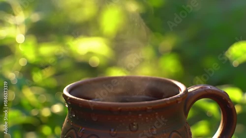 Steaming drink in nature; beverage relaxes outdoors with greenery bokeh