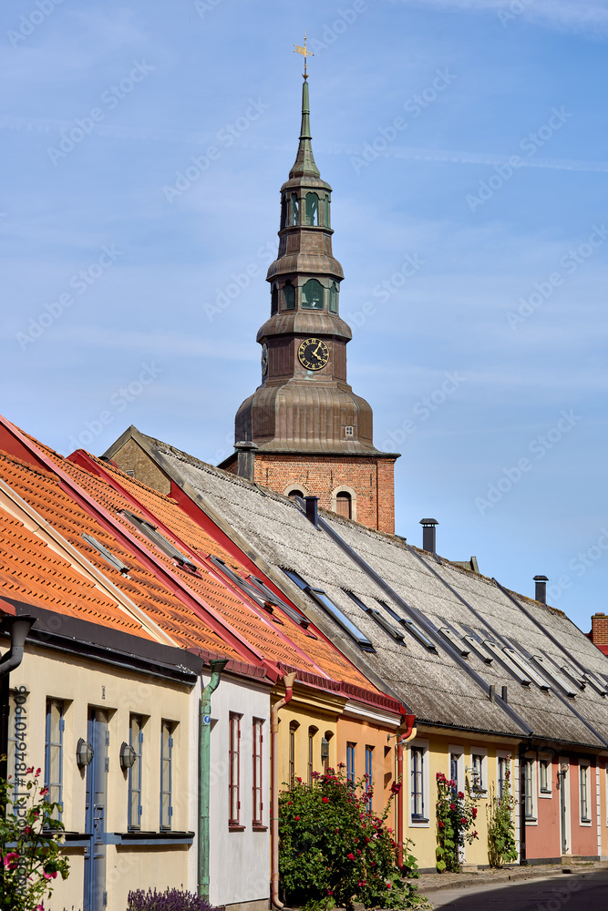 Fototapeta premium Colorful get of historic houses with the church or cathedral bell tower towering above the village roofs on a sunny day in Ystad, Sweden. Relaxed Scandinavian small town travel, high quality of life