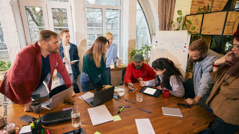 Fototapeta premium Startup team working together around table in modern office. Concept of creative startup teamwork, internal discussion and collaborative work process.