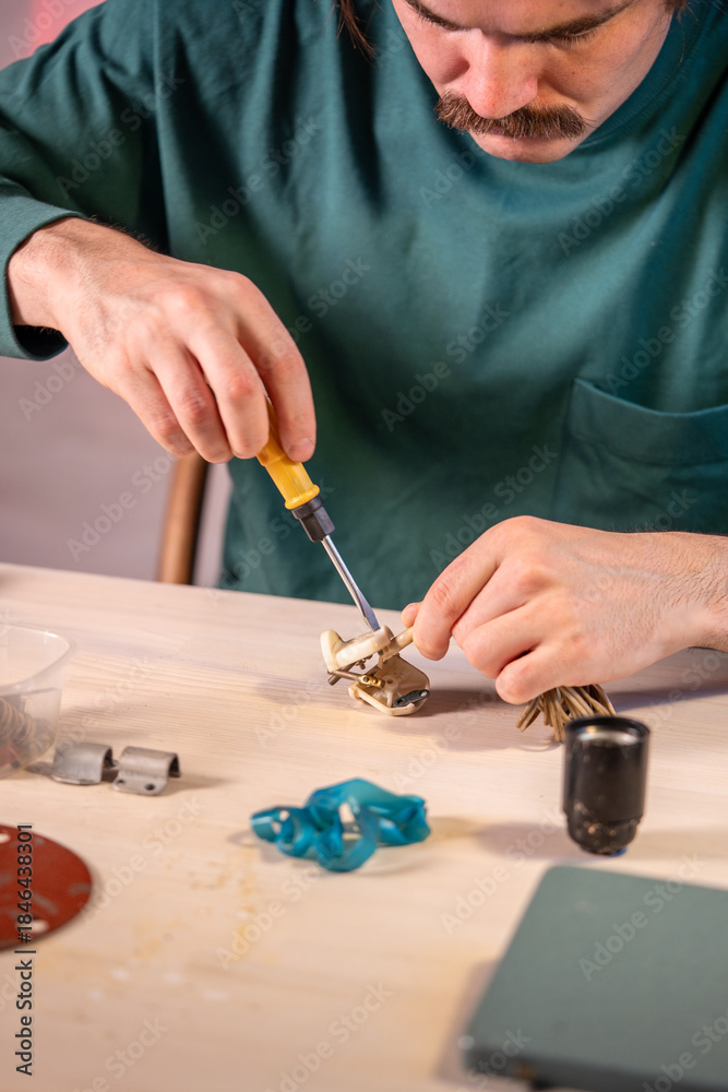 Fototapeta premium Man technician working at table in workshop, disassembling old plug casing from vintage electrical lamp using screwdriver tool, unscrewing parts and components, removes screws for future repairing.