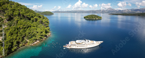 Aerial view of a luxury yacht anchored near a lush, green island with swimmers enjoying the crystal-clear turquoise waters, Sipanska Luka, Dubrovnik-Neretva County, Croatia.