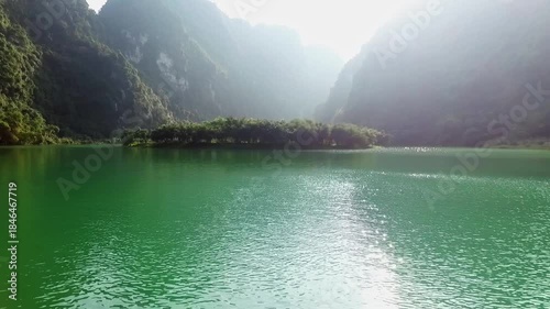 A drone flies over the Trang an Valley, a large body of water, with mountains covered in dense forest to the right and left.