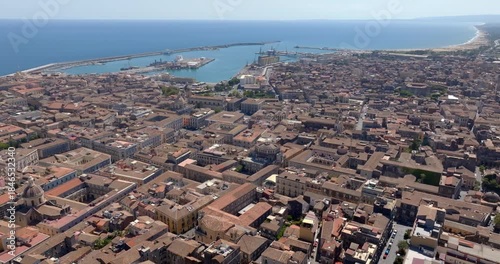 Aerial view of the city of Catania, Italy. It is the second largest city in Sicily. In the background, at horizon, there are the city port and the Mediterranean Sea. It is sunny summer morning.