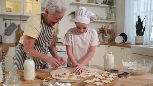 Happy family in kitchen. Grandmother granddaughter child cutting cookies of dough on kitchen table together. Grandma teaching kid girl cook bake cookies. Household teamwork helping family generations