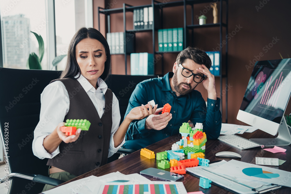 Fototapeta premium Two professionals work with colorful building blocks and charts at a busy modern office desk