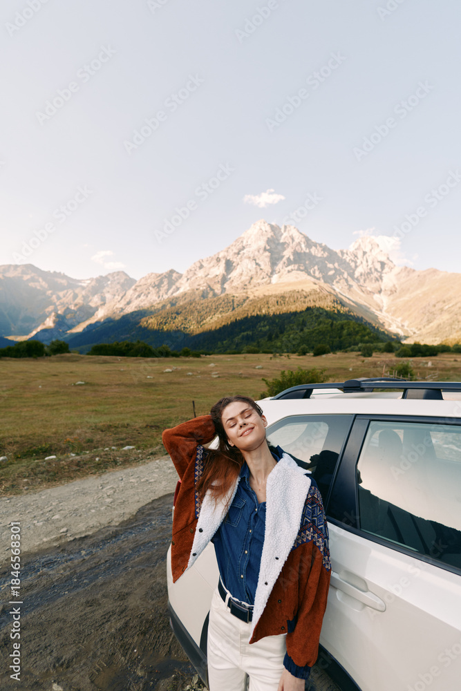 Fototapeta premium Woman by car in mountains and nature, travel portrait on road and meadow. Young woman leaning on SUV, relaxed pose, scenic alpine landscape and sunny outdoor adventure.