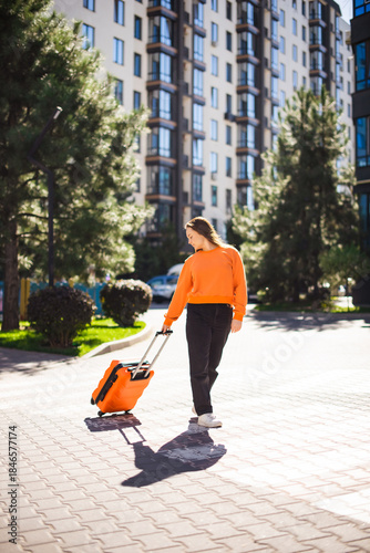 woman with orange suitcase walking on street to relocate another city