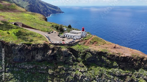 Aerial 4K drone footage of dramatic coastal cliffs and lighthouse viewpoint on Madeira island, overlooking the deep blue Atlantic Ocean and rugged shoreline in clear daylight.